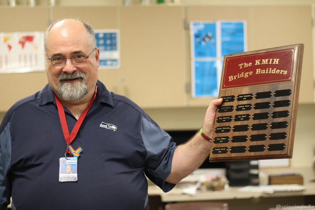 High school radio station KMIH's General Manger Joe Bryant stands in radio classroom holding plaque that reads "The KMIH Bridge Builders." Photo: J. Waits/Radio Survivor