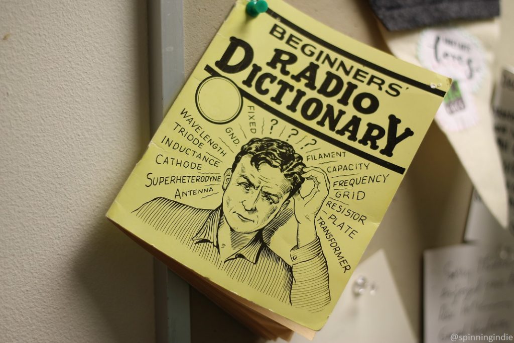 Beginners' radio dictionary posted on bulletin board at KBCS. Has drawing of man scratching his head, surrounded by radio terms: antenna, superheterodyne, cathode, etc. Photo: J. Waits/Radio Survivor