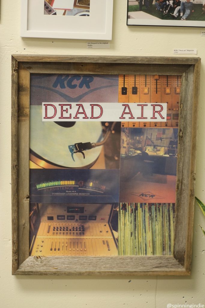 Framed copy of KCR college radio's magazine "Dead Air" on wall of station. Cover image is collage of station photos, including a piece of spinning white vinyl, sound board photos, photo of LPs, and a vintage studio photo. Photo: J. Waits/Radio Survivor