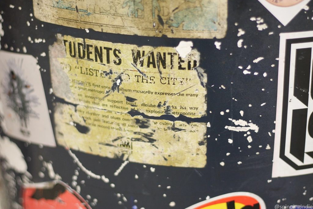 Sticker-covered table at KSDT. Sticker in center is old and faded, reads: "TUDENTS WANTED TO "LISTE...THE CITY"...." Photo: J. Waits/Radio Survivor