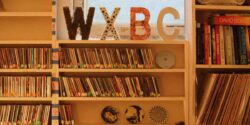 Photo of college radio station WXBC in 2022. WXBC in block letters atop bookshelves full of CDs. Photo: J. Waits