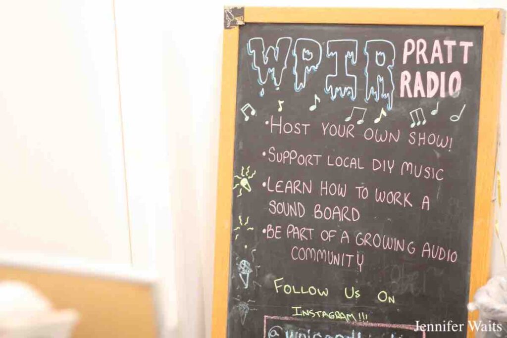 Photo of chalkboard sign at college radio station WPIR Pratt Radio in March, 2023. Sign reads: WPIR Pratt Radio. Host your own show! Support local DIY music. Learn how to work a sound board. Be part of a growing audio community. Follow us on Instagram!!!! Photo: J. Waits