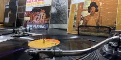 Turntable with vinyl record playing and Alice's Restaurant album cover in the background. Photo by J. Waits