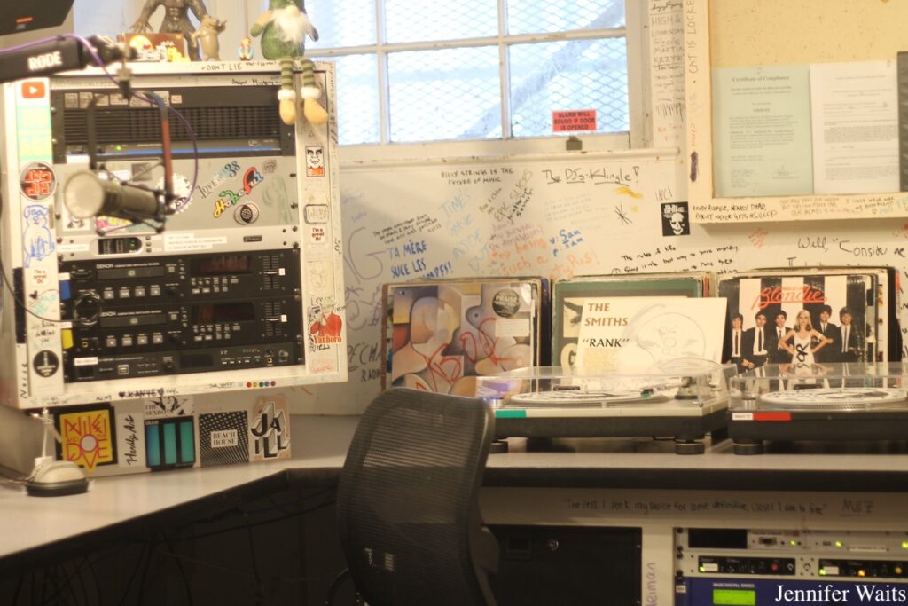 Bowdoin College radio station WBOR's studio. Radio equipment can be seen, including two turntables, CD players, and a microphone. Behind the turntables are vinyl records, including a Blondie record and a Smiths record. Photo: J. Waits