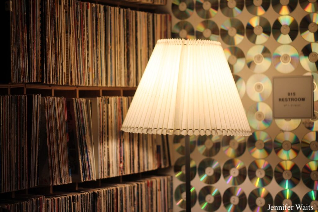 Bowdoin College radio station WBOR. Pictured: shelves full of vinyl records, CDs decorating a wall, an illuminated lamp, and a restroom sign. Photo: J. Waits