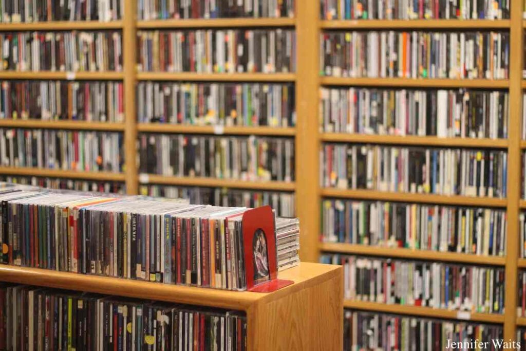 Photo of CD library at college radio station WONY. An entire wall is filled with shelves packed with CDs and a shelving unit in the foreground has CDs inside and on top of it. Photo: J. Waits