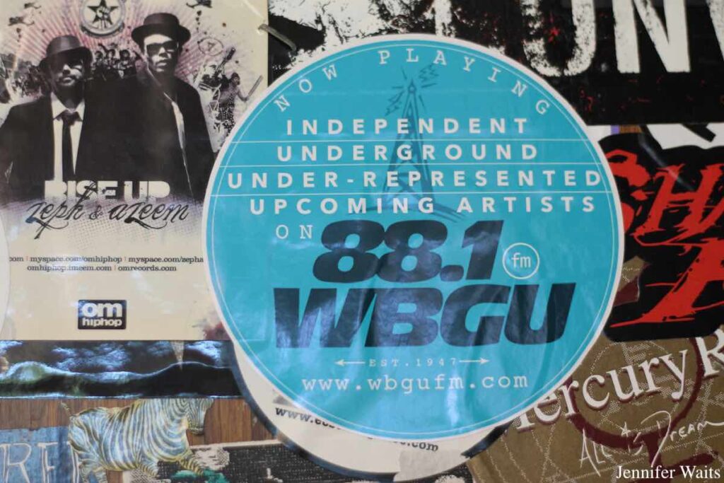 Photo of stickers on old door at college radio station WBGU-FM. Center sticker reads "now playing independent underground under-represented upcoming artists on 88.1 FM est. 1947  WBGU www.wbgufm.com." Photo: J. Waits