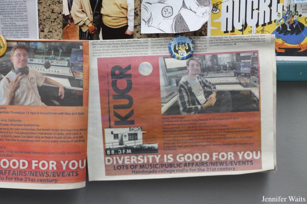 Photo of bulletin board at college radio station KUCR. Attached to the board are photos, artwork, and newspaper clippings of ads for KUCR featuring DJ profiles. Photo: J. Waits